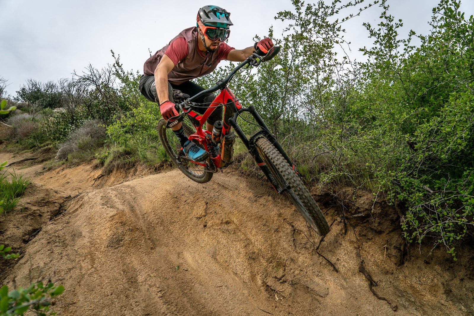 Mountain Biker sends it over a jump wearing The Drop MTB custom biking apparel and mountain biking gear.   Launching a mountain bike off a jump while wearing The Drop MTB custom Mountain biking jersey and mountain biking shorts and biking gloves.